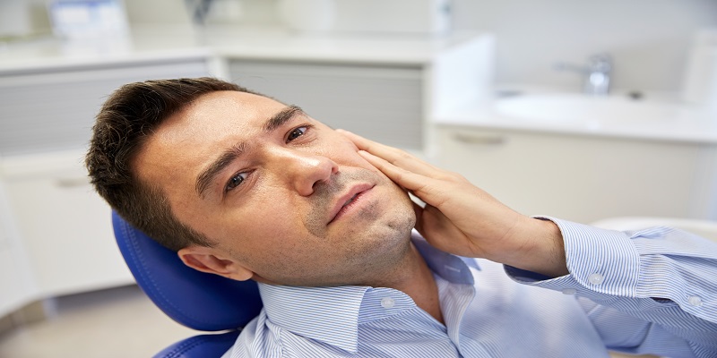 people, medicine, stomatology and health care concept - unhappy male patient having toothache sitting on dental chair at clinic office